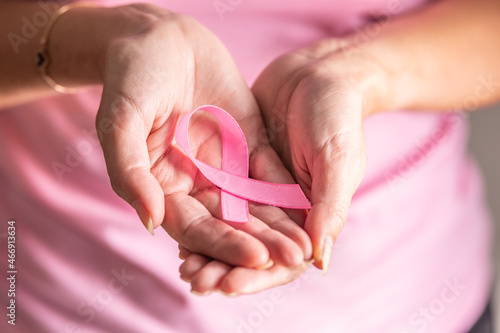 Detail of woman holding pink ribbon in her folded palms  the symbol of breast cancer prevention need