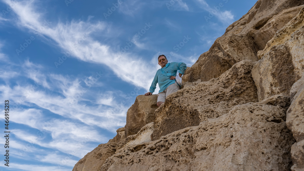 A fragment of the wall of the ancient pyramid of Cheops. On huge ancient boulders, against a background of blue sky and clouds, there is a smiling man. Close-up. Egypt. Giza