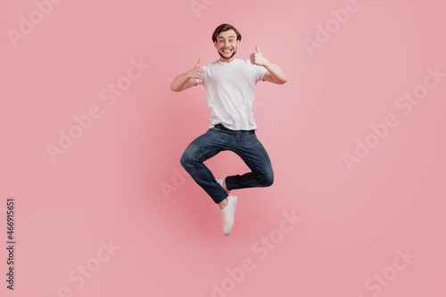 Full size photo of young happy excited smiling positive man jump show thumb-up like cool advert isolated on pink color background