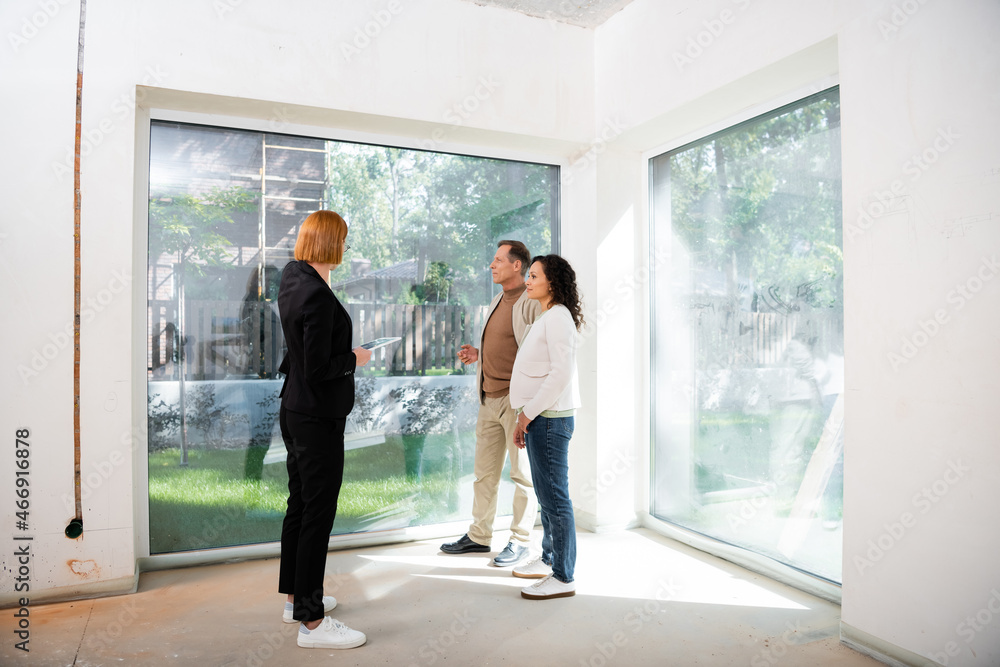 redhead realtor holding digital tablet near interracial couple inside of new house redhead realtor holding digital tablet near interracial couple inside of new house