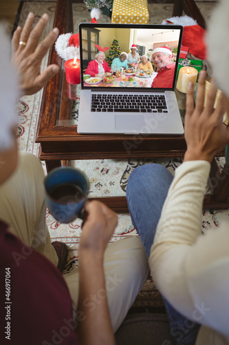 Two men waving to smiling diverse senior friends in santa hats on laptop christmas video call screen