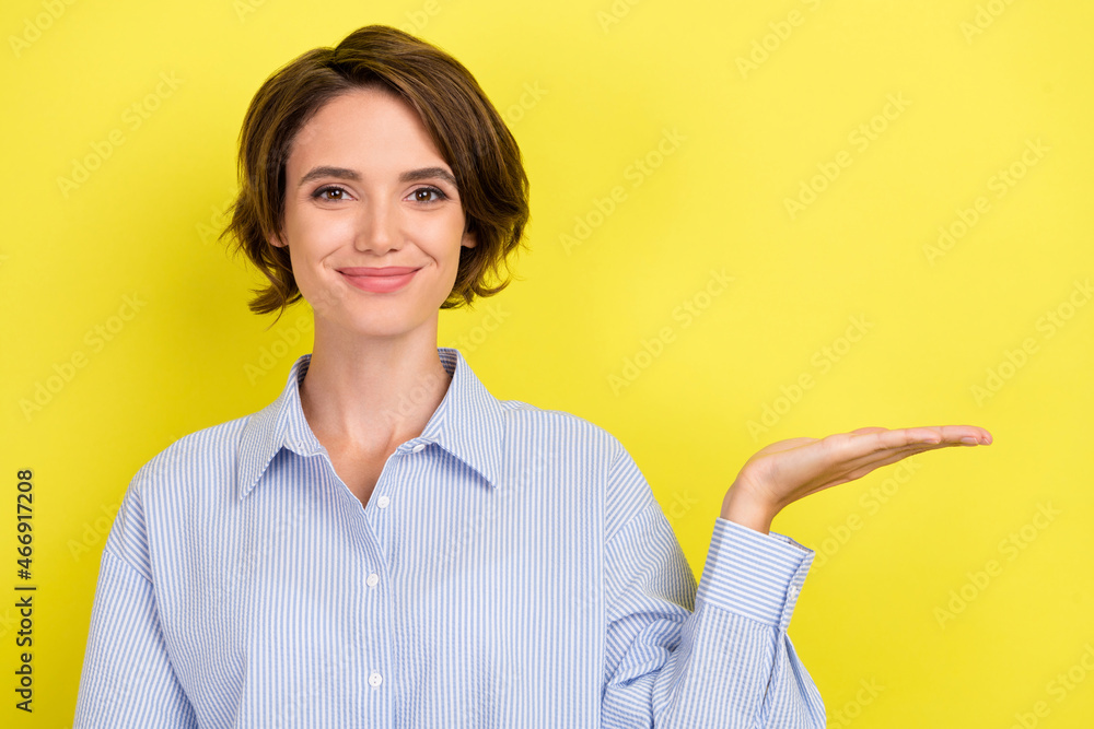 Photo of young attractive woman happy positive smile hold hand product offer advertise isolated over yellow color background Photo of young attractive woman happy positive smile hold hand product offer advertise isolated over yellow color background