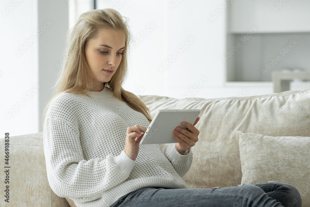 Happy pregnant woman uses a digital tablet while sitting on the sofa in the living room Happy pregnant woman uses a digital tablet while sitting on the sofa in the living room
