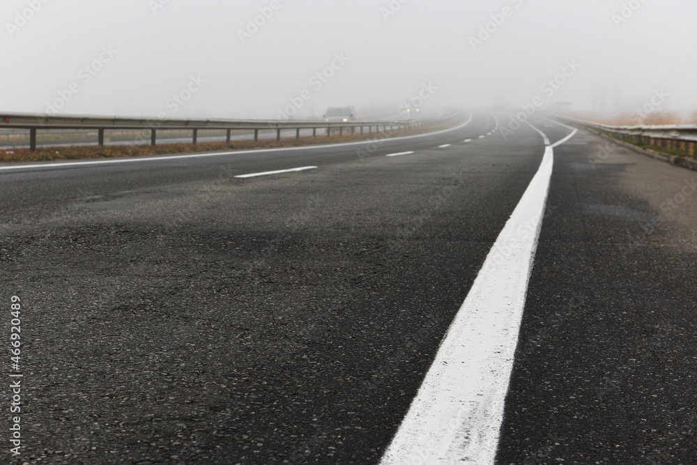 Obraz premium Asphalt road with a white stripe in the fog.
