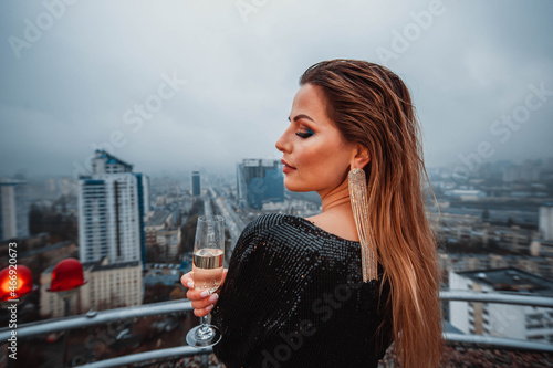 Woman in long black dress holding a glass of champagne on the rooftop in the rain 