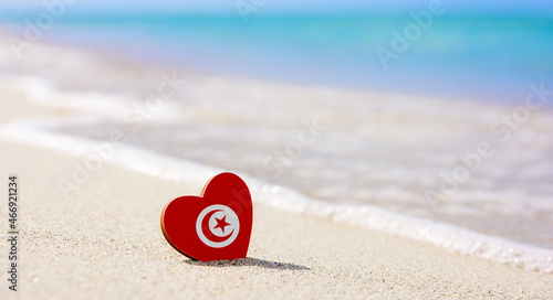 Flag of Tunisia in the shape of a heart on a sandy beach. The concept of the best vacation in Tunisia