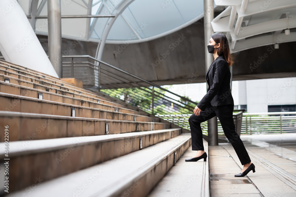 A woman wearing a black suit and trousers is walking up stairs outdoors.