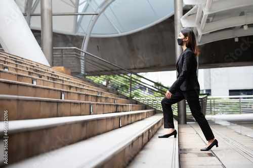 A woman wearing a black suit and trousers is walking up stairs outdoors. © MPIX.TURE