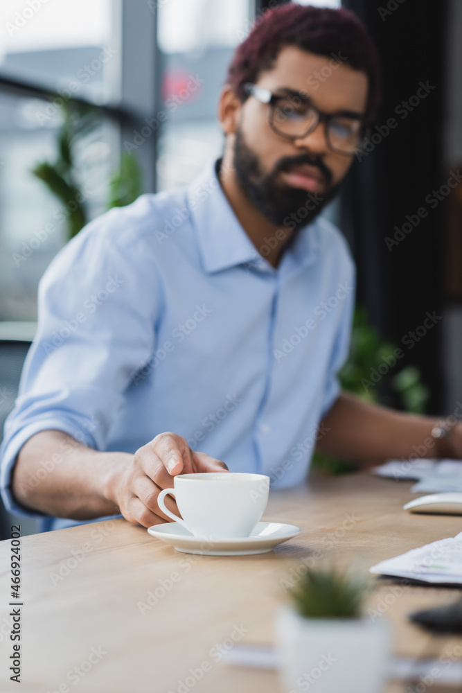 Cup of coffee on table near blurred african american businessman in office