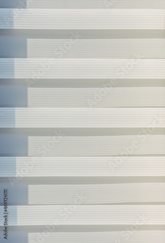 Abstract geometric horizontal lines white and gray gradient color. Repeating pattern, background texture, design of striped lines. Roller blinds illuminated by the sun, close-up.