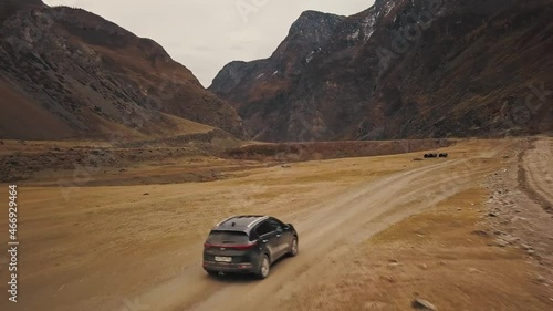 A black SUV jeep car is driving along an empty country road in the huge Katu-Yaryk canyon Chulyshman Valley with a large mountain bubbling river. Altai, Siberia, Russia. People travel along a dirt