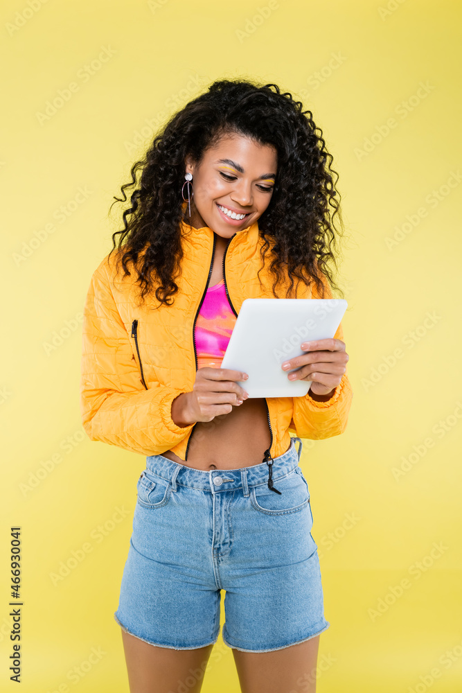 positive african american young woman using digital tablet isolated on yellow positive african american young woman using digital tablet isolated on yellow
