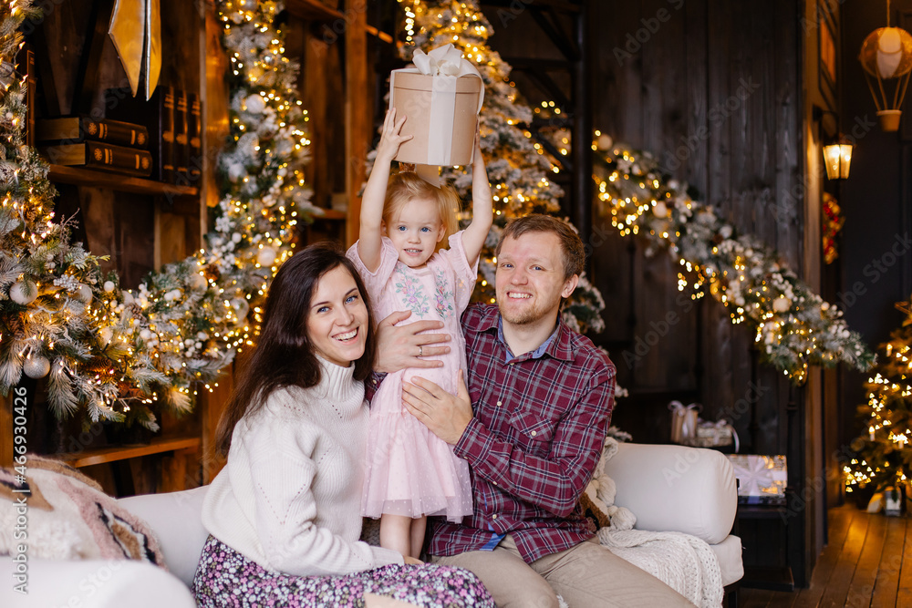 A full family celebrates Christmas at home. Nice and cozy loft interior with garlands. Happy parenting. Christmas spirit. Warm holiday atmosphere. Togetherness new year mood. Parents give a gift