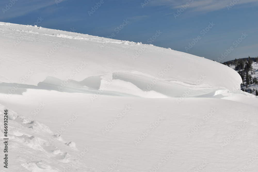 Große Schneeverwehung, Schneewechte hängt über tief verschneiter Fläche vor blauem Himmel im Gebirge