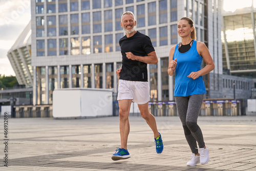 Cheerful mature couple, man and woman exercising and jogging together in the city on a warm summer day