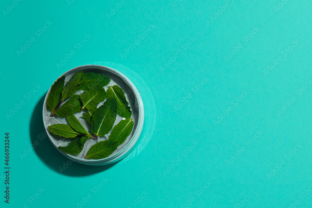 Cooling body and massage cream decorated with fresh mint leaves on a turquoise background. Place for your text. View from above. Cooling body and massage cream decorated with fresh mint leaves on a turquoise background. Place for your text. View from above.