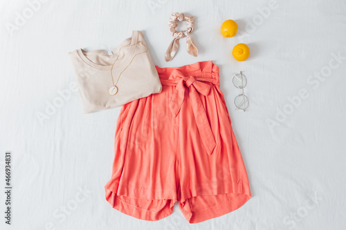 Summer female fashion stylish composition. Shorts, t shirt, lemons, glasses, scrunchie and necklace on white messy bed sheet background. Flat lay, top view.