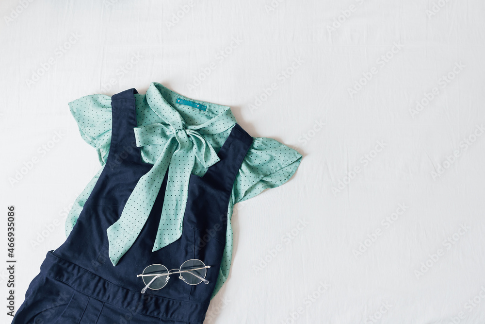 Feminine spring and summer fashion composition with dark blue overalls on white bed sheet background. Flat lay, top view. Vintage clothes collage. Female fashion blog and social media concept. Feminine spring and summer fashion composition with dark blue overalls on white bed sheet background. Flat lay, top view. Vintage clothes collage. Female fashion blog and social media concept.