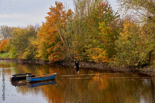 atumn scenery of the canal "Käseburger Sieltief" in Brake Unterweser (Germany) with colorful trees, a blue boat and a black dressed Halloween skeleton on a swing for decoration