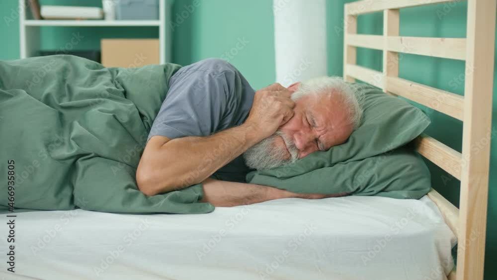 Elderly Man Tries to Rest, Gets Annoyed By Noisy Neighbors, Suffers From Insomnia on the Bed at Home. Thin Walls, Apartment Without Soundproofing, Renovation Work From Neighbors. Neighborhood Concept. Elderly Man Tries to Rest, Gets Annoyed By Noisy Neighbors, Suffers From Insomnia on the Bed at Home. Thin Walls, Apartment Without Soundproofing, Renovation Work From Neighbors. Neighborhood Concept.