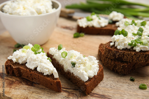 Bread with cottage cheese and green onion on wooden table, closeup