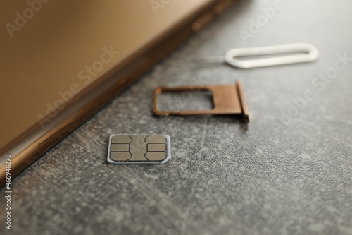 SIM card, mobile phone, tray and ejector tool on grey table, closeup