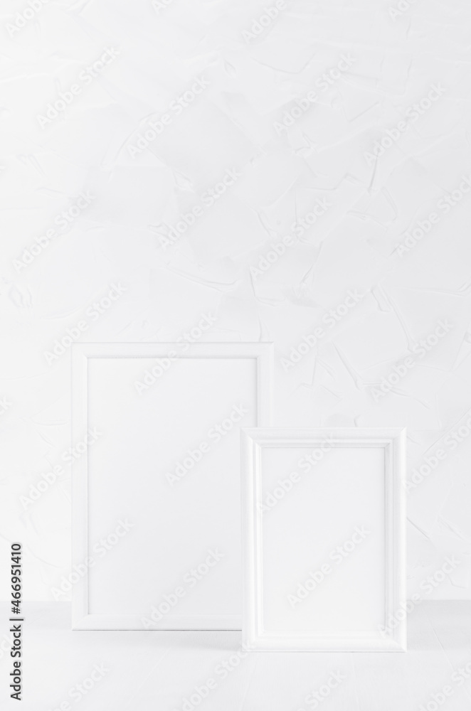 Two different size white wood blank rectangle photo frames in soft light interior on wood floor and plaster wall, copy space, vertical. Template for presentation, portfolio, text, design, advertising. Two different size white wood blank rectangle photo frames in soft light interior on wood floor and plaster wall, copy space, vertical. Template for presentation, portfolio, text, design, advertising.