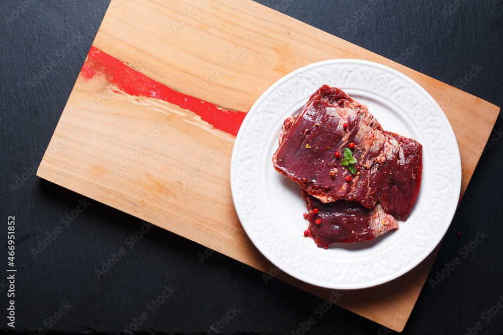 Food concept Fresh raw Skirt steak in white flat ceramic plate on wooden board and black slate stone board with copy space Food concept Fresh raw Skirt steak in white flat ceramic plate on wooden board and black slate stone board with copy space