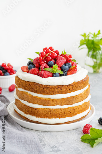 Homemade naked layered vanilla cake with whipped cream and fresh berries on top on a gray concrete background. Summer cake. Copy space.