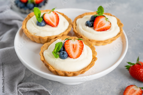 Delicious mini tarts with fresh berries and custard on a white plate on a gray concrete background. Copy space