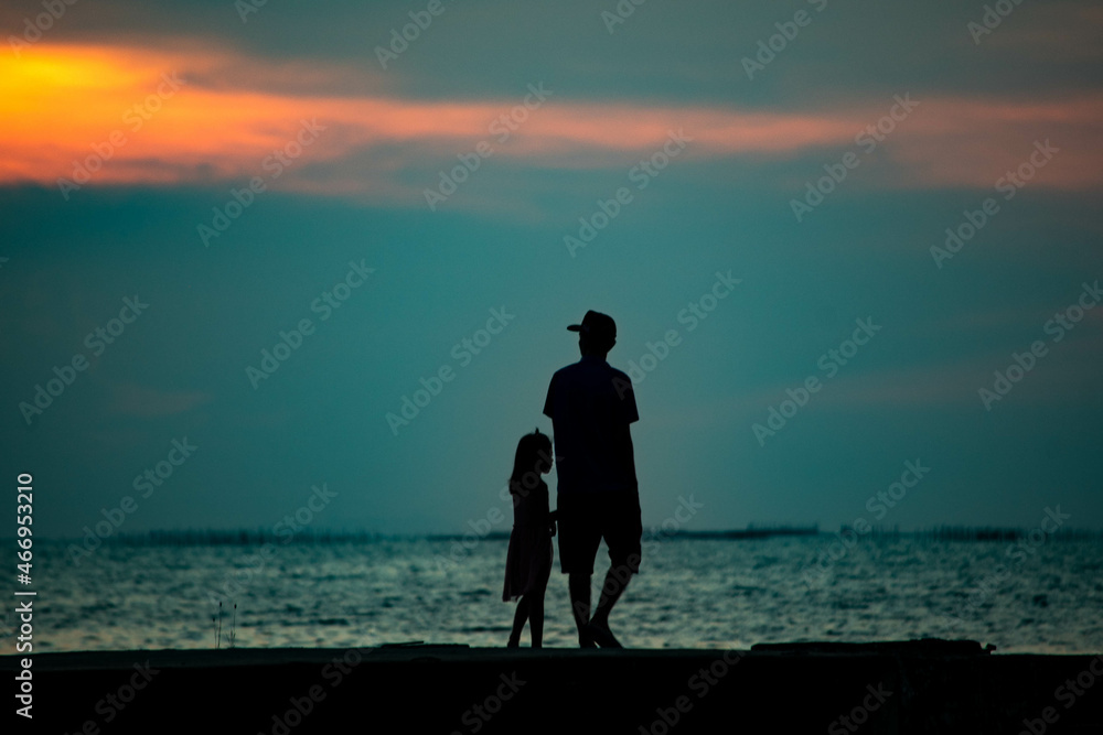 Silhouette of father and daughter walking at sunset on the cement bridge at Chittaphawan Temple, Thailand