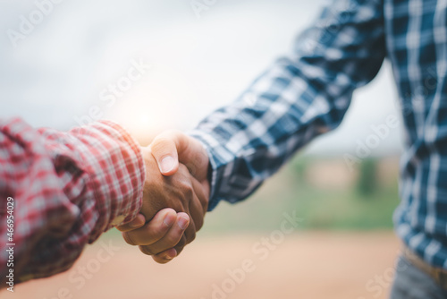 Two businessmen shaking hands in field with tractor working in background. Agribusiness concept