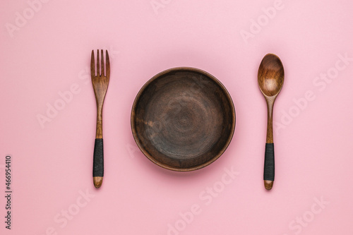 Foto Wooden spoon and fork and clay bowl on pink background