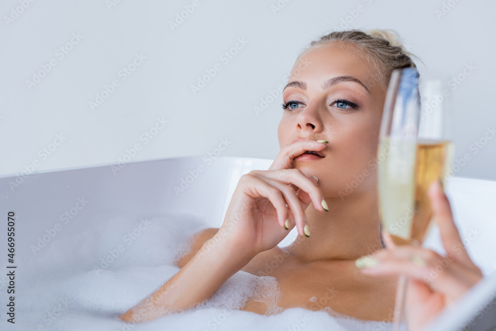 young dreamy woman taking bath and holding blurred glass of champagne young dreamy woman taking bath and holding blurred glass of champagne