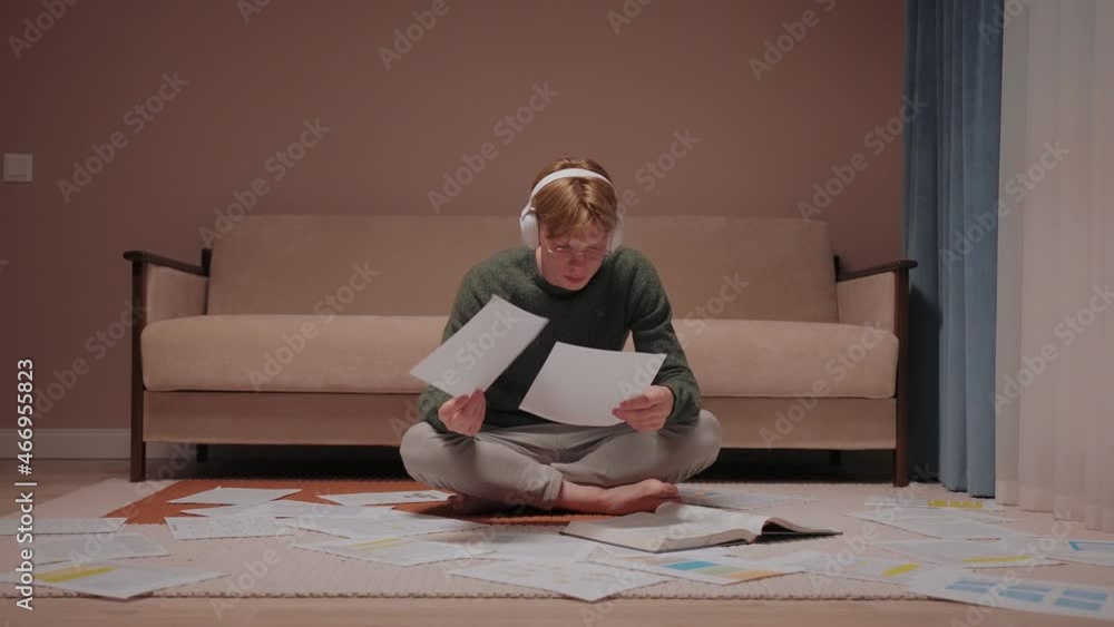 Stressed guy sits on the floor full of papers and gives up, leaning on couch. Guy studying in warm color room. Giving up doing homework in the evening. High quality 4k footage Stressed guy sits on the floor full of papers and gives up, leaning on couch. Guy studying in warm color room. Giving up doing homework in the evening. High quality 4k footage