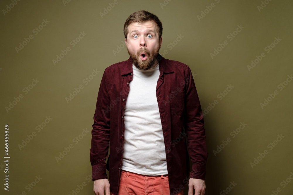 Handsome bearded man is amazed, he opens mouth in surprise and looks with big eyes. Green background. Handsome bearded man is amazed, he opens mouth in surprise and looks with big eyes. Green background.