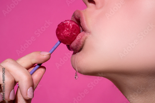 Orgasm concept. Lollipop in the mouth, close-up. Beautiful girl mouth with lolli pop. Glossy red woman lips with tongue. Mouth lick suck chupa chups isolated on pink.