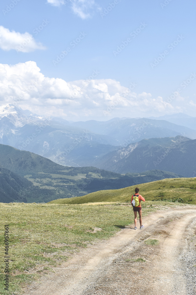 Female hiker on a trail in Svaneti region, Georgia, Asia. Summer mountain landscape with snowcapped mountains in the background. Blue sky with clouds above. Georgian tourist destination