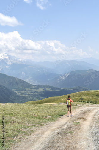Female hiker on a trail in Svaneti region, Georgia, Asia. Summer mountain landscape with snowcapped mountains in the background. Blue sky with clouds above. Georgian tourist destination © ppohudka