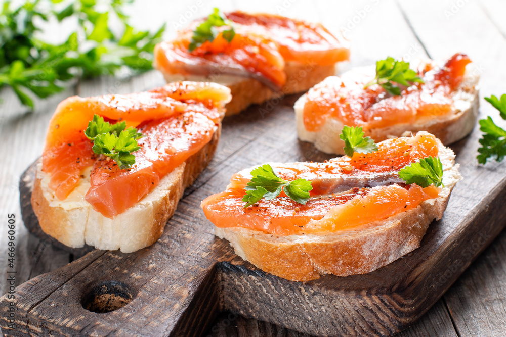 Slices of fresh baguette with butter and salmon served on wooden board on wood table Slices of fresh baguette with butter and salmon served on wooden board on wood table