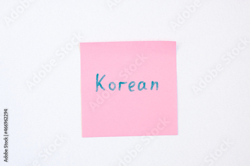 Top view flat lay of the reminder notepaper of pink color with word Korean on it on white background. Flashcards and language studies concept