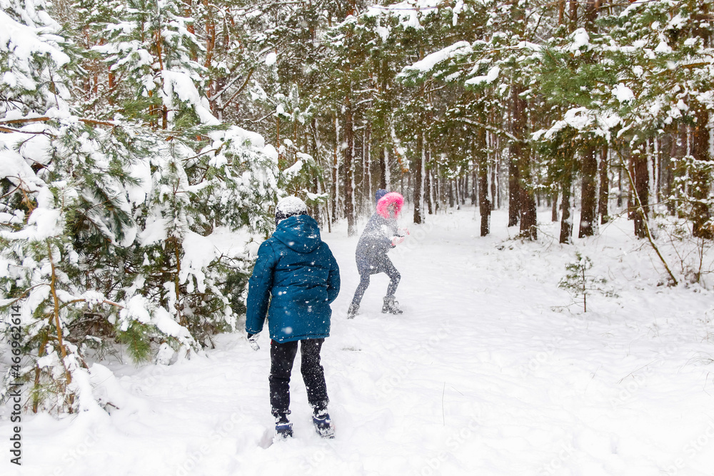 The boy throws a snowball at the girl. Funny children in Winter Park playing snowballs, actively spending time outdoors. Winter snowy woodland. Cold frost weather in snowstorm. Tween. Sibling