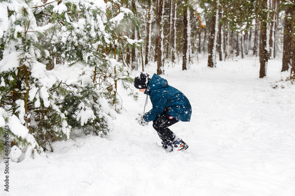 Preteen child boy in winter forest in snowstorm. Kid on snowy winter background playing snowball. Actively spending time outdoors. Winter woodland. Cold frost weather in snowstorm. Happy childhood