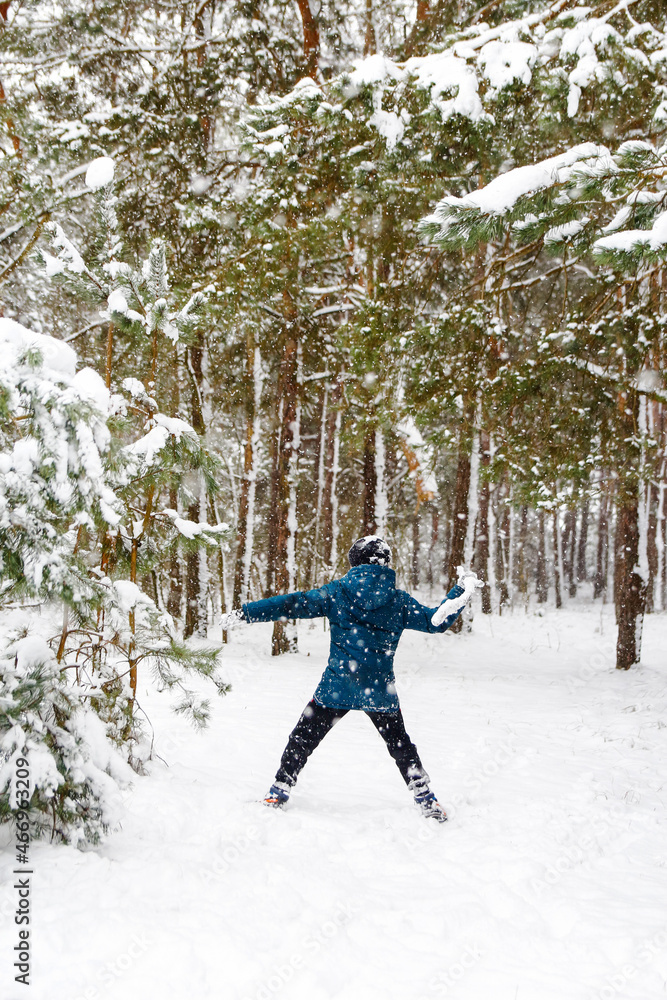 Preteen child boy in winter forest in snowstorm. Kid on snowy winter background playing by stick. Actively spending time outdoors. Winter woodland. Cold frost weather in snowstorm. Active wintertime