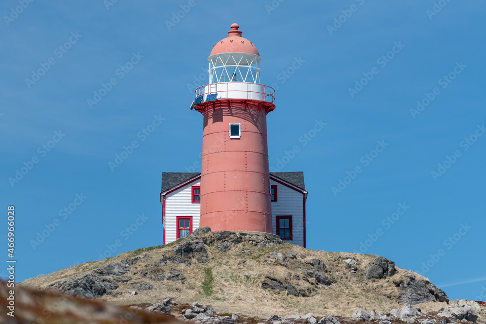 The top of a vintage lighthouse tower with a round red metal roof.  In the center of the lighthouse is a vintage lamp made of multiple pieces of glass. On top of the tower is a red metal wind arrow.