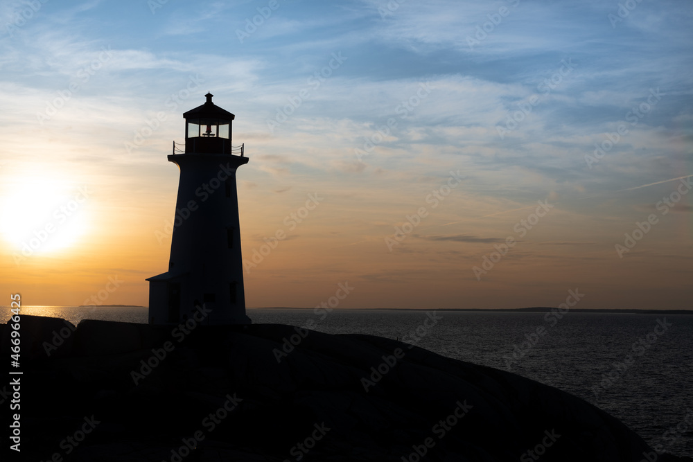 Lighthouse tower made of white concrete hexagonal, six-sided tapering concrete. The structure stands on a rock cliff. The sky has an orange color sunset. There's a green lantern in the cupola. 