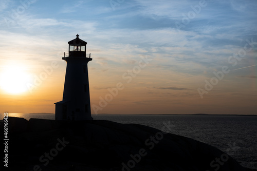Lighthouse tower made of white concrete hexagonal, six-sided tapering concrete. The structure stands on a rock cliff. The sky has an orange color sunset. There's a green lantern in the cupola. 