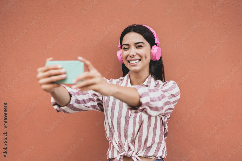 Influencer latin girl streaming live video using mobile phone while wearing wireless headphone Influencer latin girl streaming live video using mobile phone while wearing wireless headphone