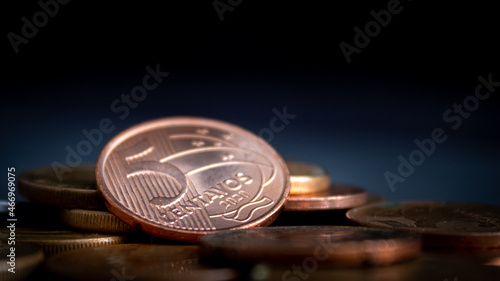 moedas empilhadas em superfície de vidro, refletindo no vidro, em um fundo escuro, com o foco em uma moeda de 5 centavos de BRL.  photo