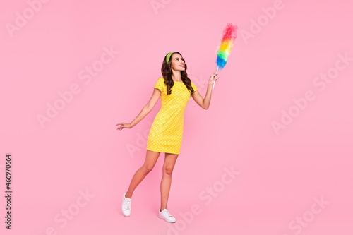 Photo of sweet adorable young lady dressed dotted dress holding duster looking empty space smiling isolated pink color background